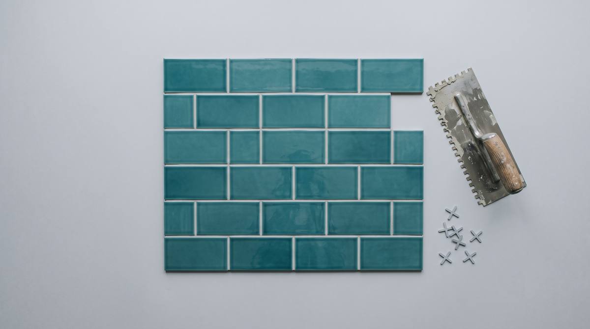 Teal subway tiles in a running-bond pattern beside a notched trowel and tile spacers